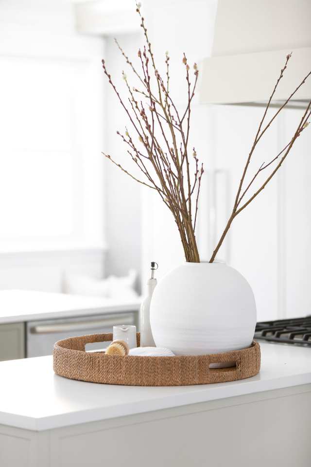 close up of all natural woven basket with cleaning supplies and vase of twigs on counter